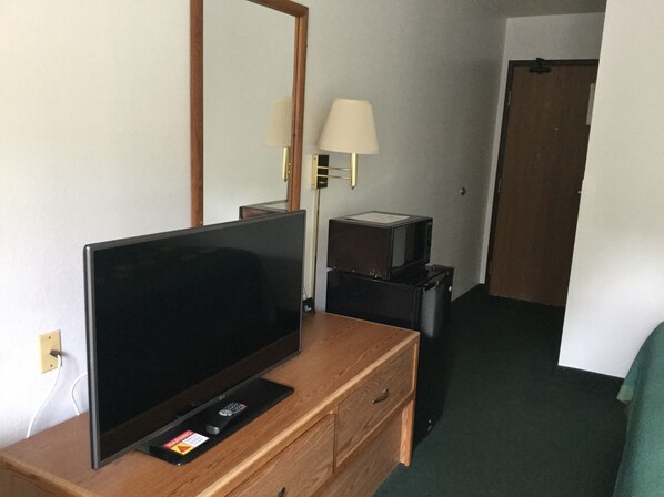 Habitación de hotel con televisor de pantalla plana sobre una cómoda de madera, una lámpara y un microondas.