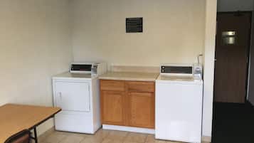 Cucina compatta con due elettrodomestici bianchi, un armadietto in legno e un cartello che indica l'uso della lavanderia per gli ospiti.