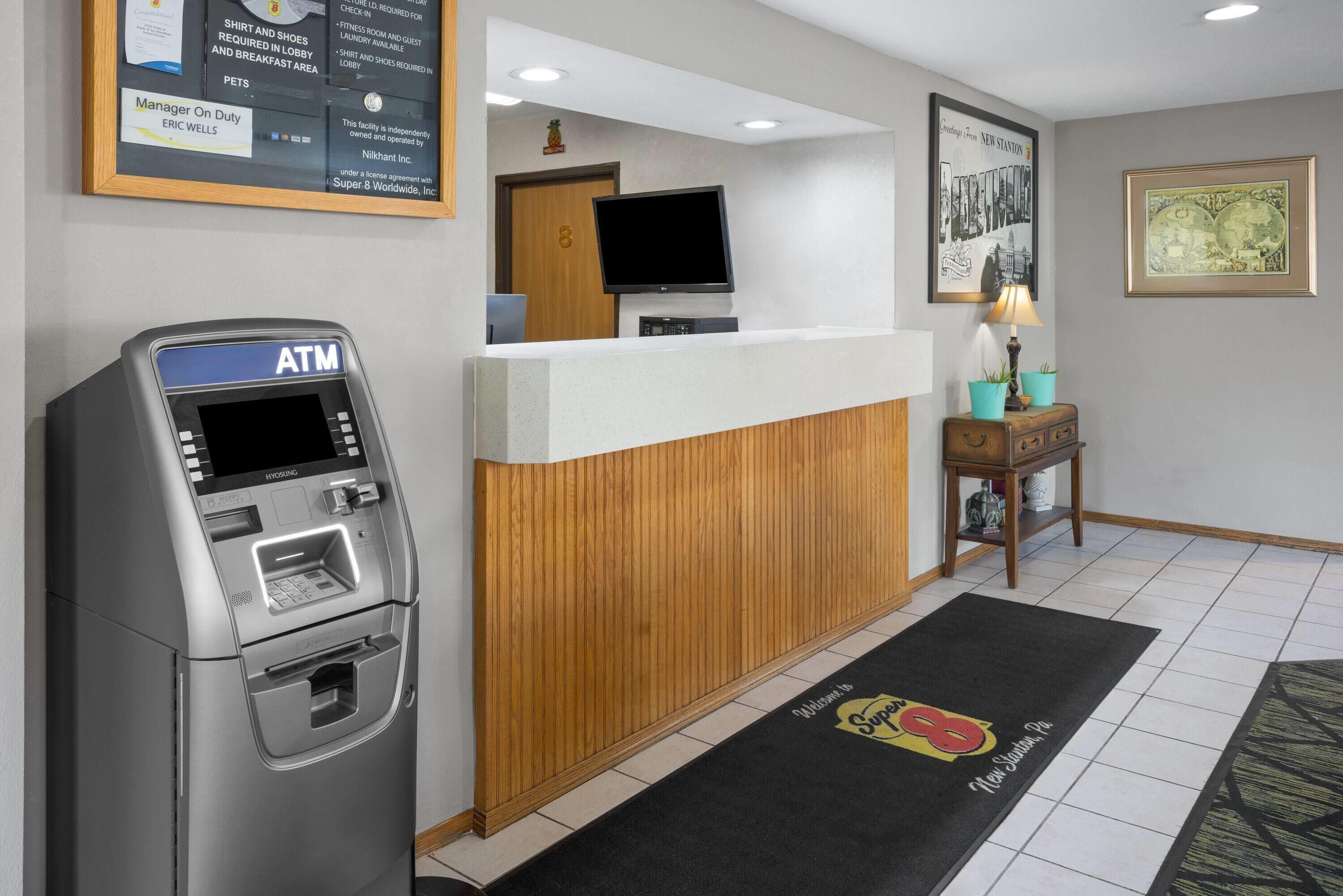 A hotel reception area with an ATM, a reception desk, a television, and a framed picture on the wall.