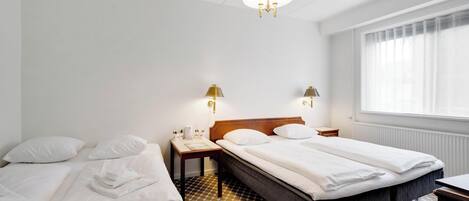 Habitación de hotel con dos camas, un ventanal con persianas, un candelabro y suelo de baldosas.