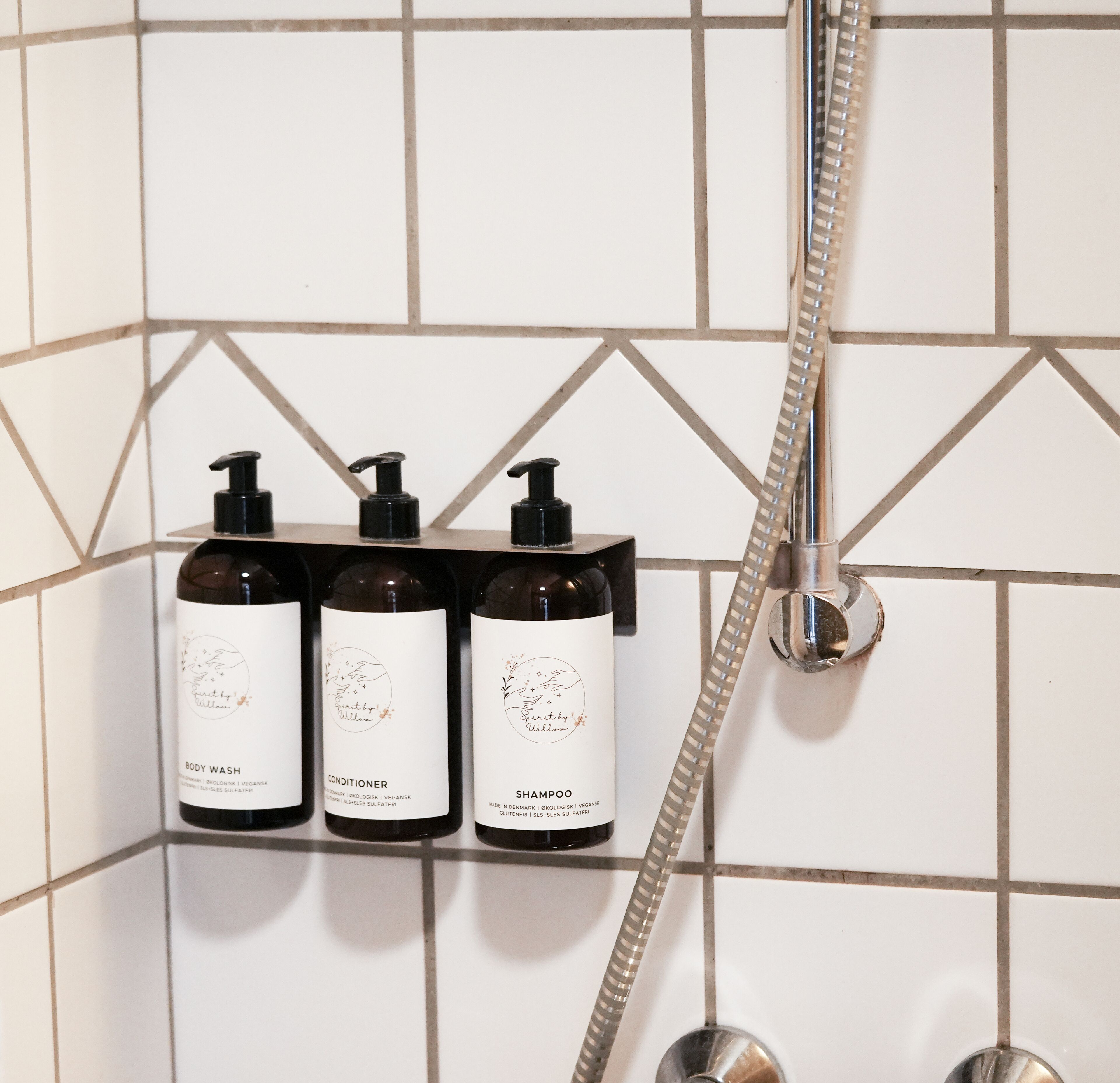 Un baño con tres botellas de jabón corporal, acondicionador y champú, y un cabezal de ducha.