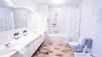 A bathroom with a large mirror, two sinks, a bathtub, and a toilet.