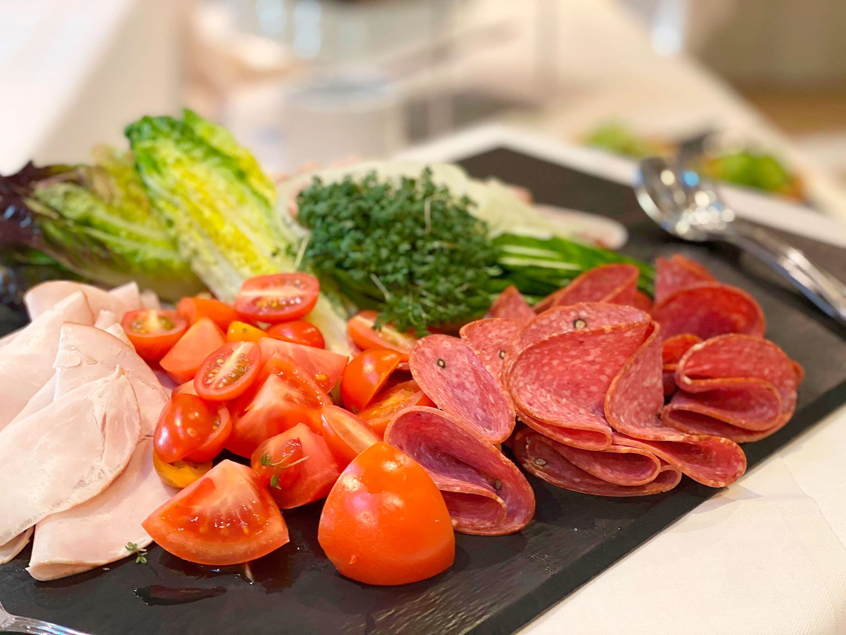 A charcuterie board with sliced meats, tomatoes, and greens.