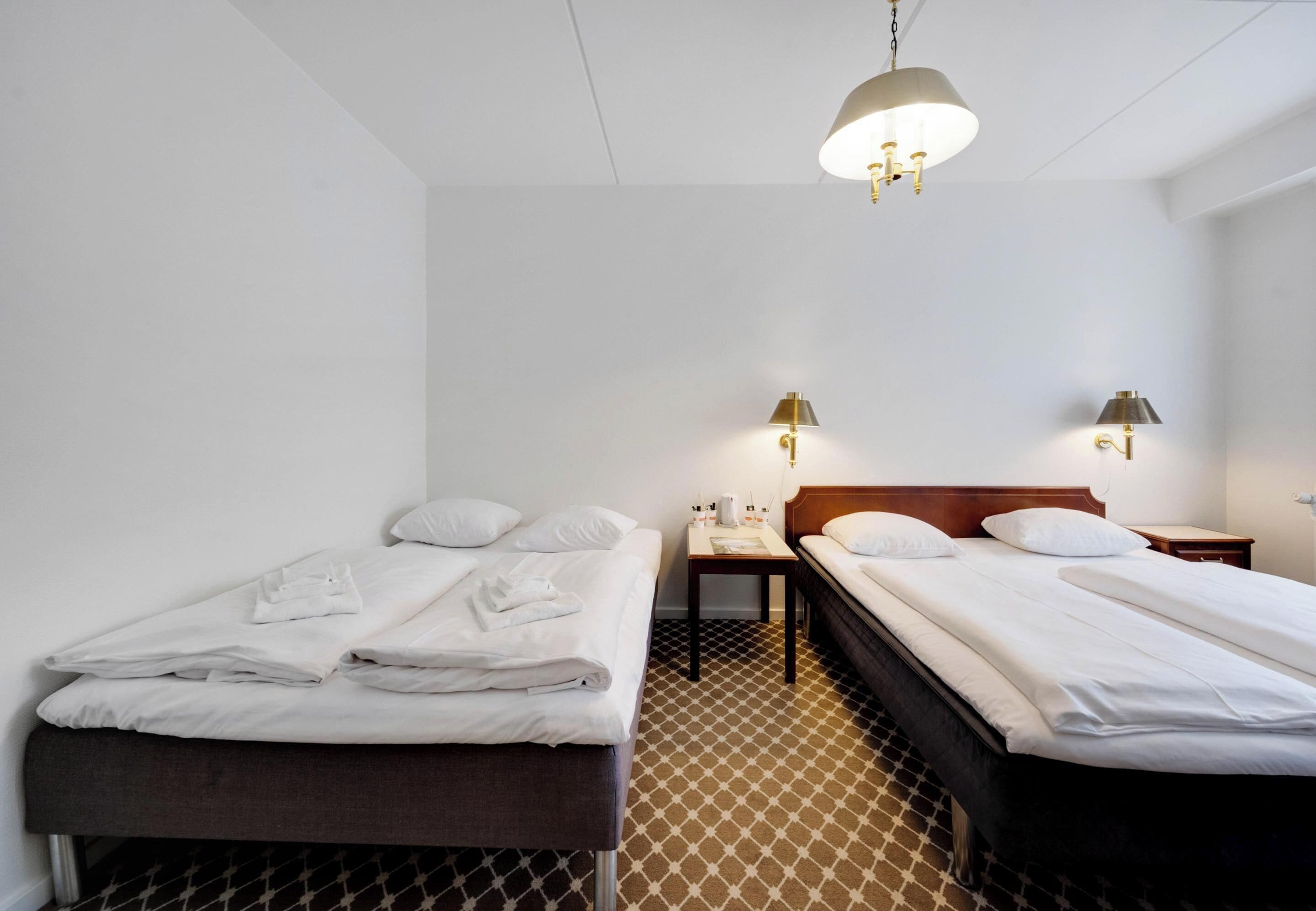 A hotel room with two beds, a small table, and two wall-mounted lamps.
