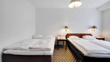 A hotel room with two beds, a small table, and two wall-mounted lamps.