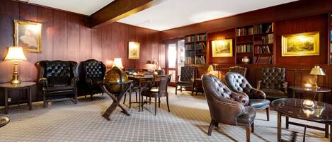 A library with leather armchairs, wooden bookshelves, and a patterned carpet.