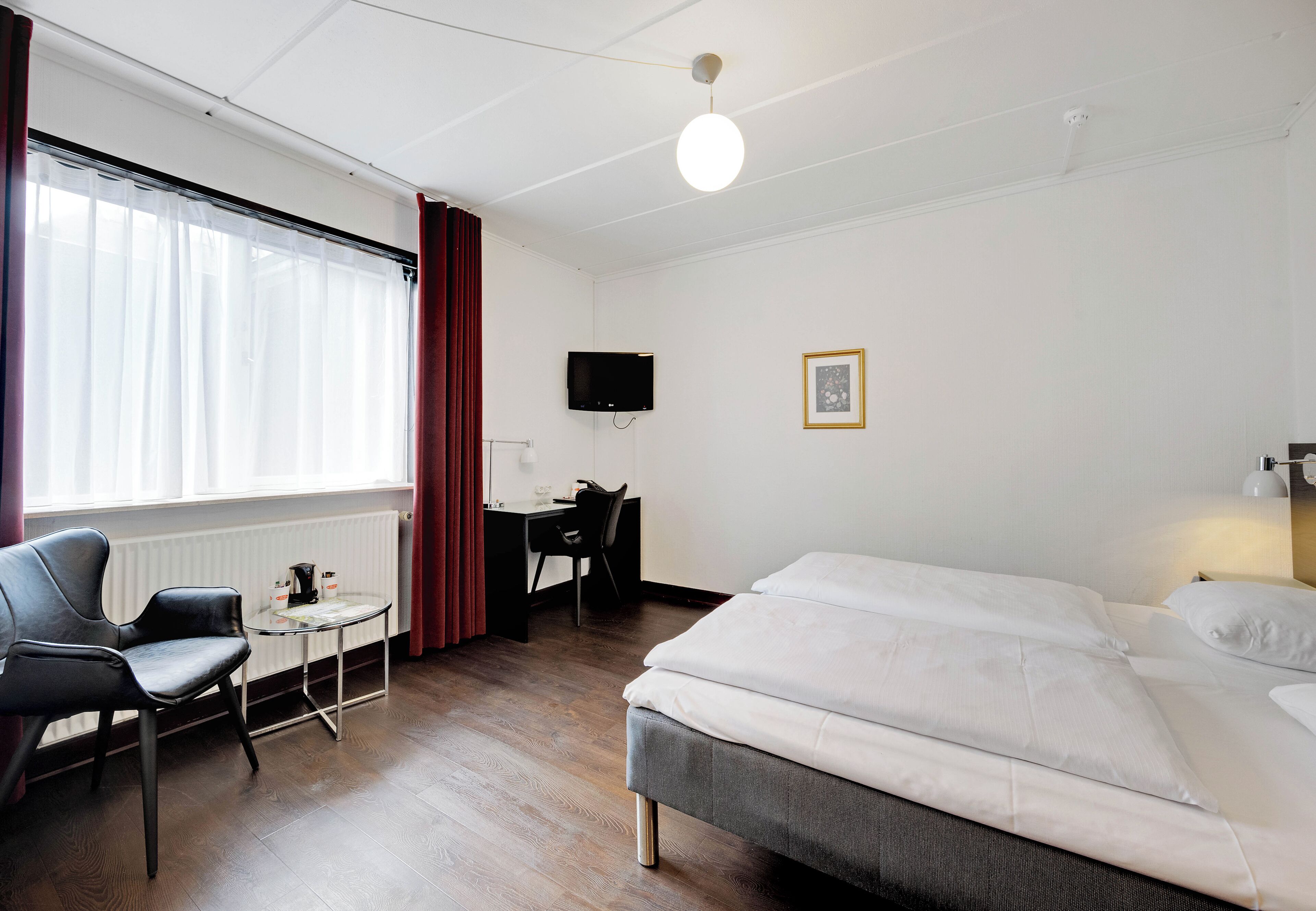 Een hotelkamer met een bed, een bureau, een stoel, een televisie en een raam met gordijnen.