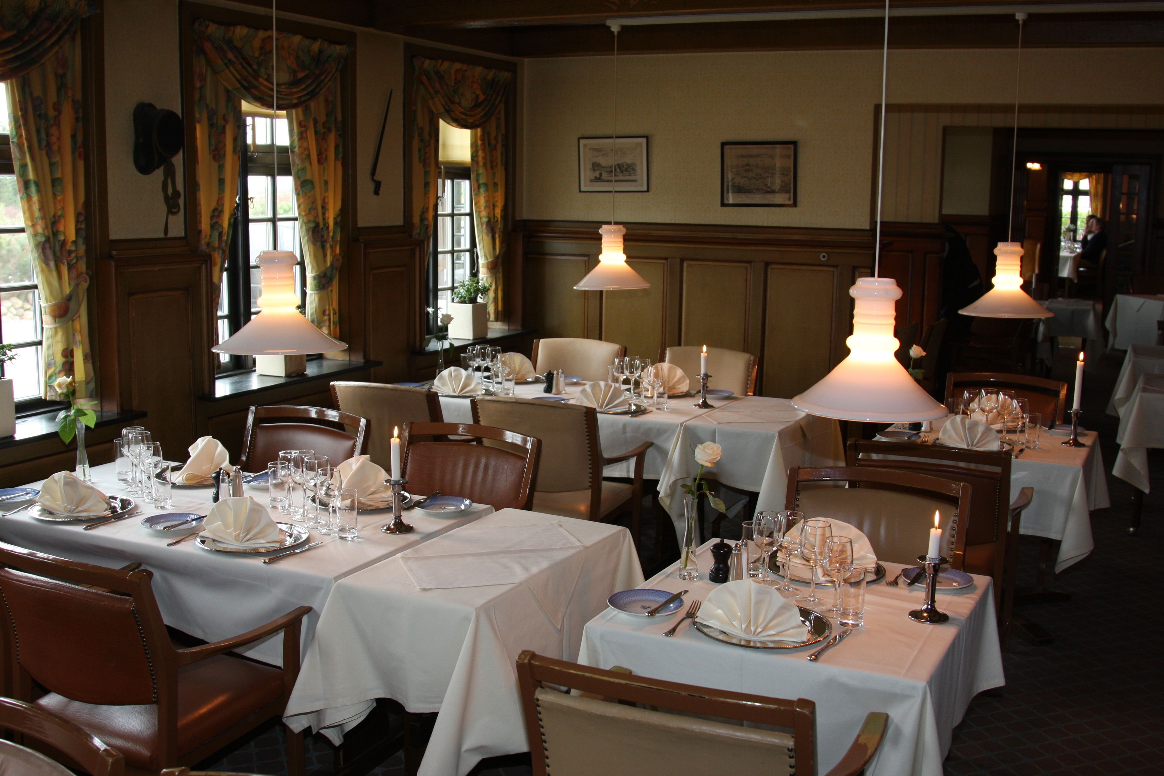 A restaurant with tables set for dining, featuring white tablecloths and candle centerpieces.