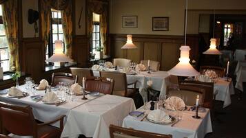 A restaurant with tables set for dining, featuring white tablecloths and candle centerpieces.