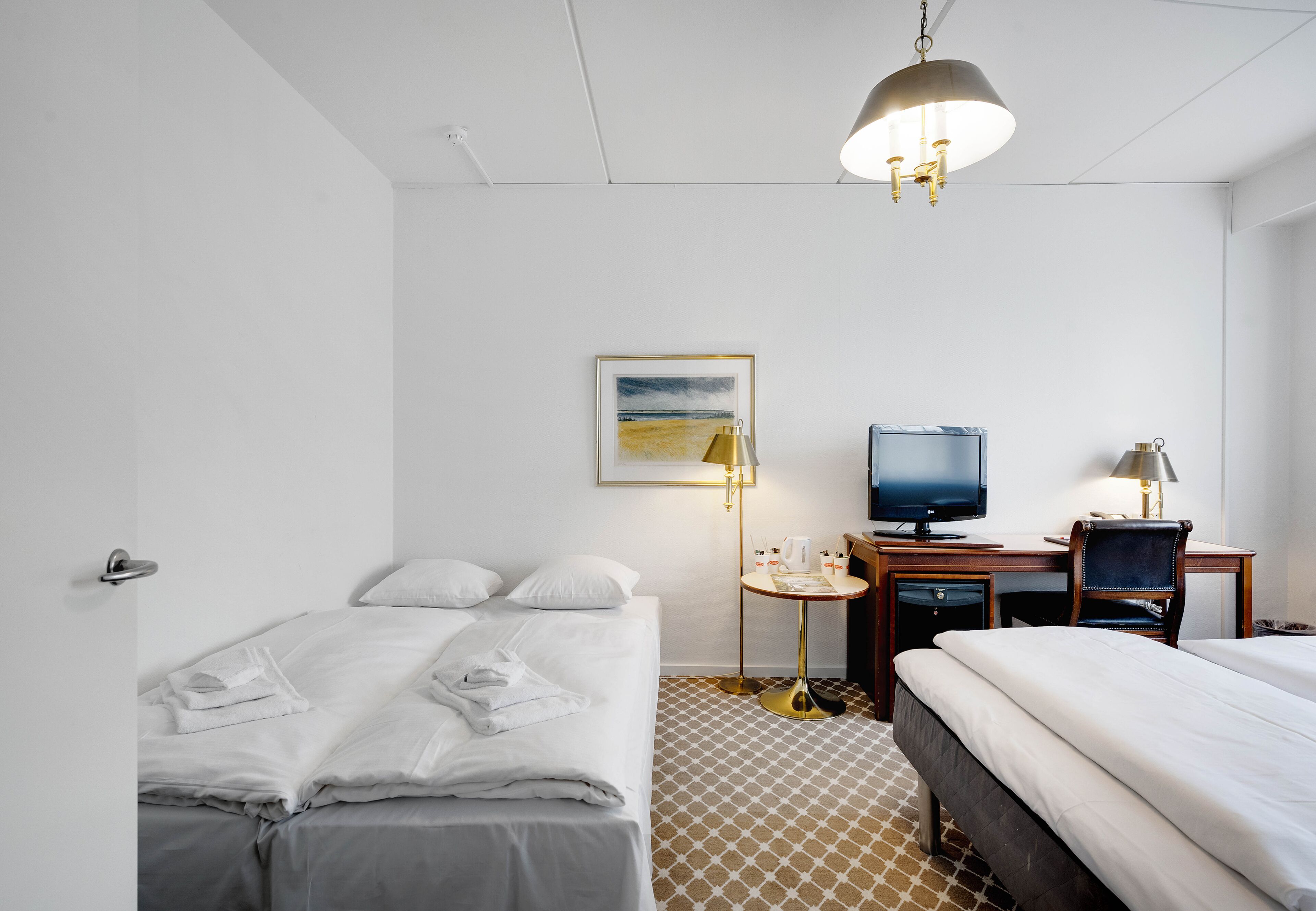 Una habitación de hotel con una cama, un escritorio con computadora, televisor y lámpara.