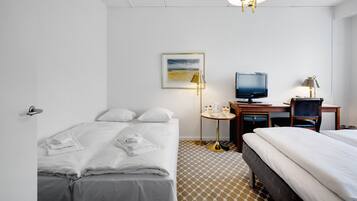 Una habitación de hotel con una cama, un escritorio con computadora, televisor y lámpara.