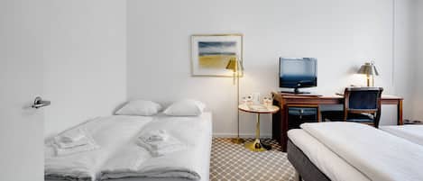 A hotel room with a bed, a desk with a computer, a television, and a lamp.