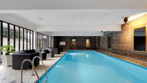 Una piscina interior con cubierta de madera, zona de estar y grandes ventanales.