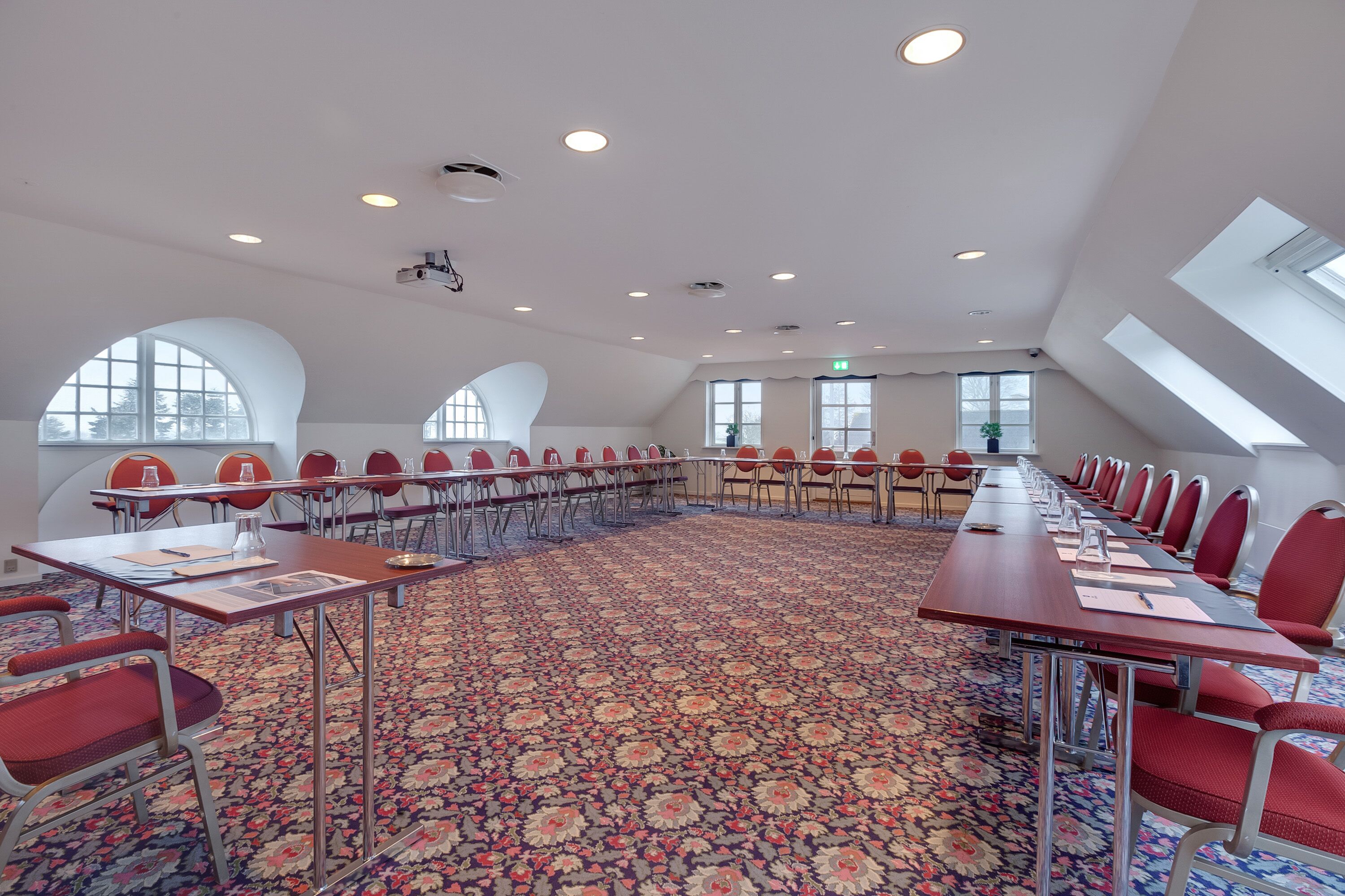 Une salle de conférence avec une longue table, des chaises rouges et un tapis à motifs.
