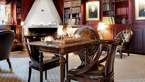 Una habitación con chimenea, estanterías, un tablero de ajedrez y muebles antiguos.