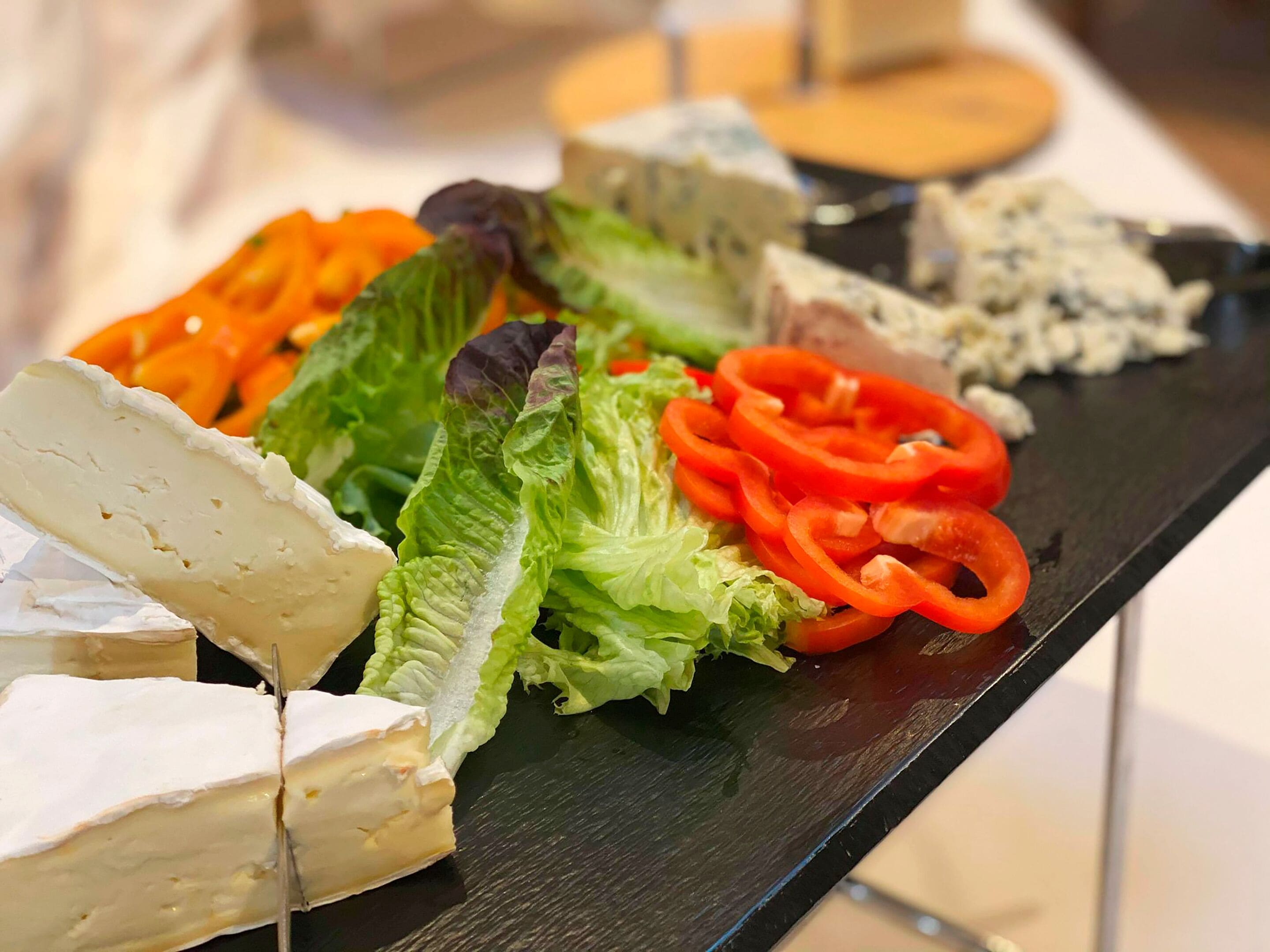 Una tabla de quesos con diferentes tipos de queso y verduras sobre una bandeja negra.
