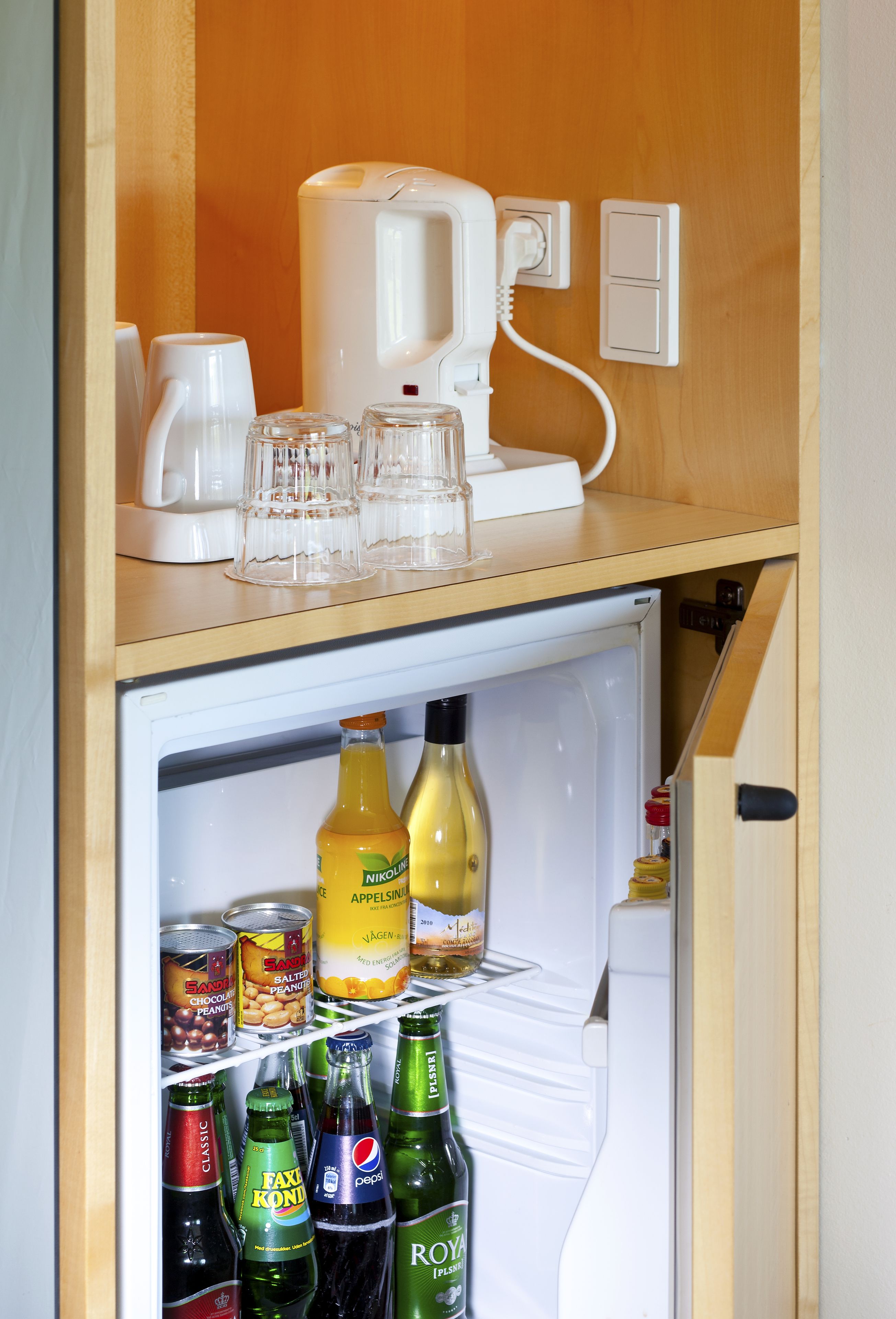 Ein kompakter Kühlschrank mit Kaffeemaschine und Gläsern auf der Oberseite, sowie verschiedenen Getränken und Snacks im Inneren.