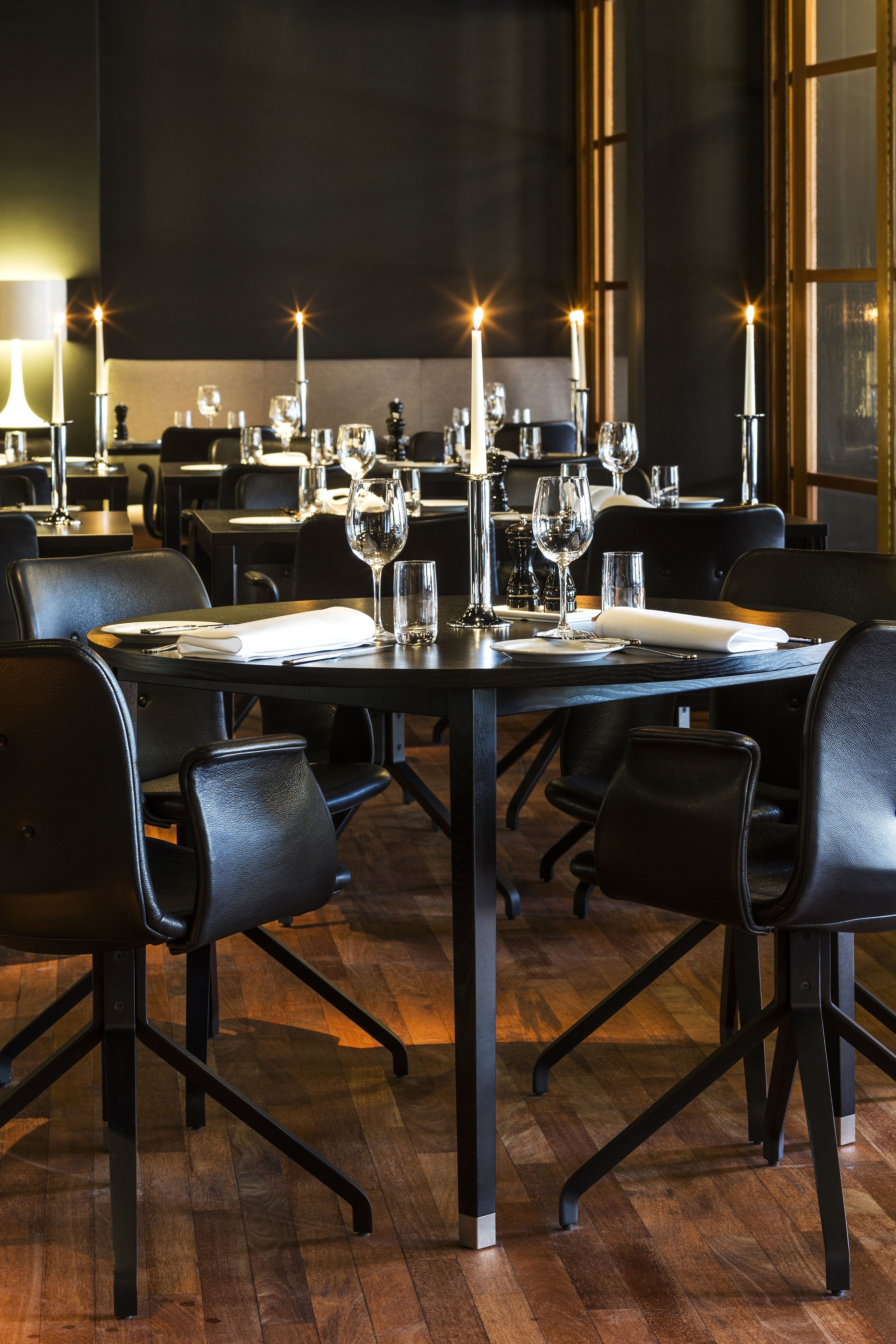 A restaurant with black leather chairs, tables set with white napkins, wine glasses, and candles.