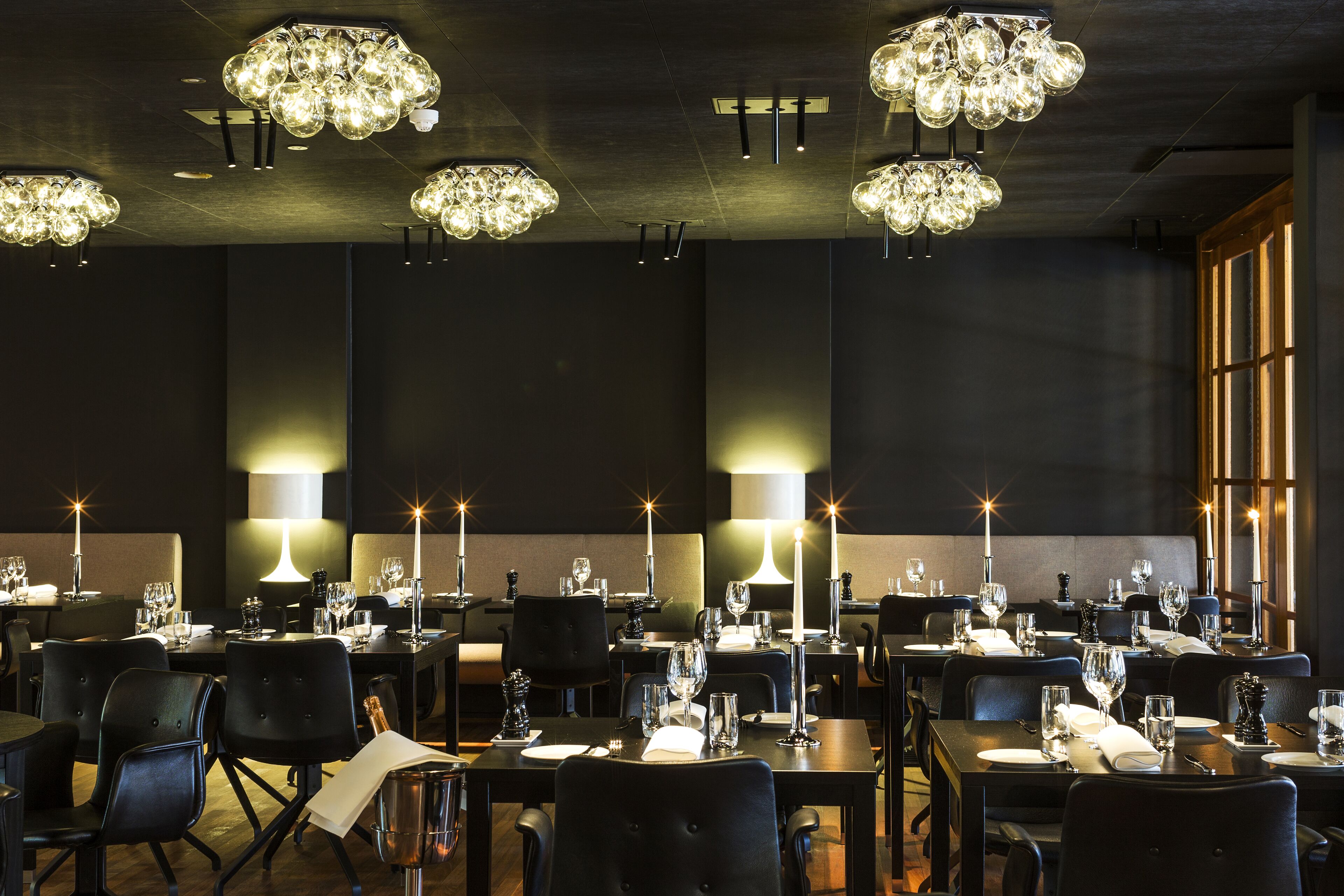 A restaurant with multiple tables set for dining, each with candles and wine glasses.