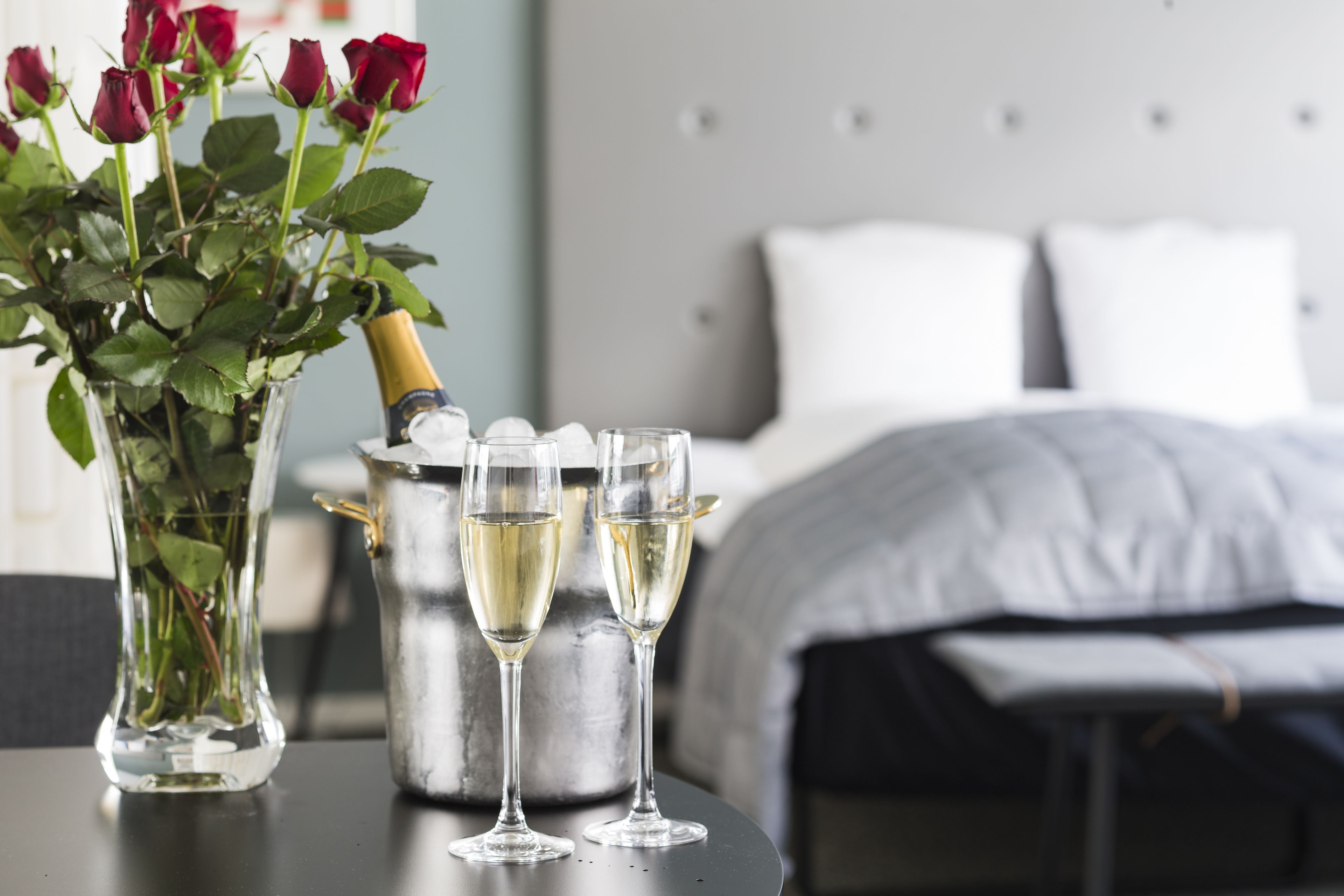 Et værelse med en seng, et natbord med en vase med roser, en champagneflaske og to champagneglas.