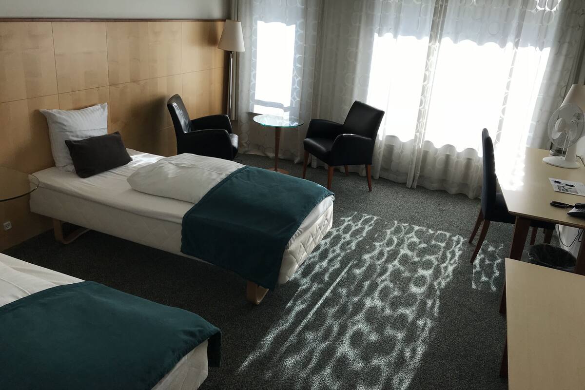 A hotel room with a bed, two chairs, a desk, and a lamp.