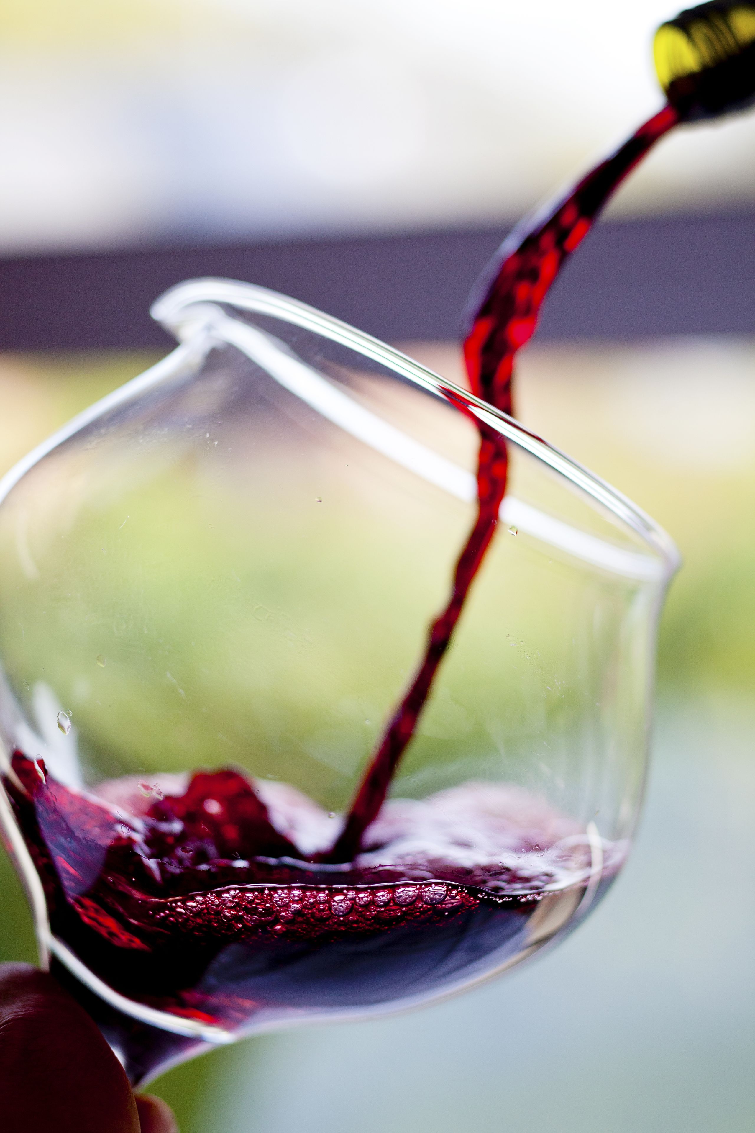 A close-up of a wine glass being filled with red wine.
