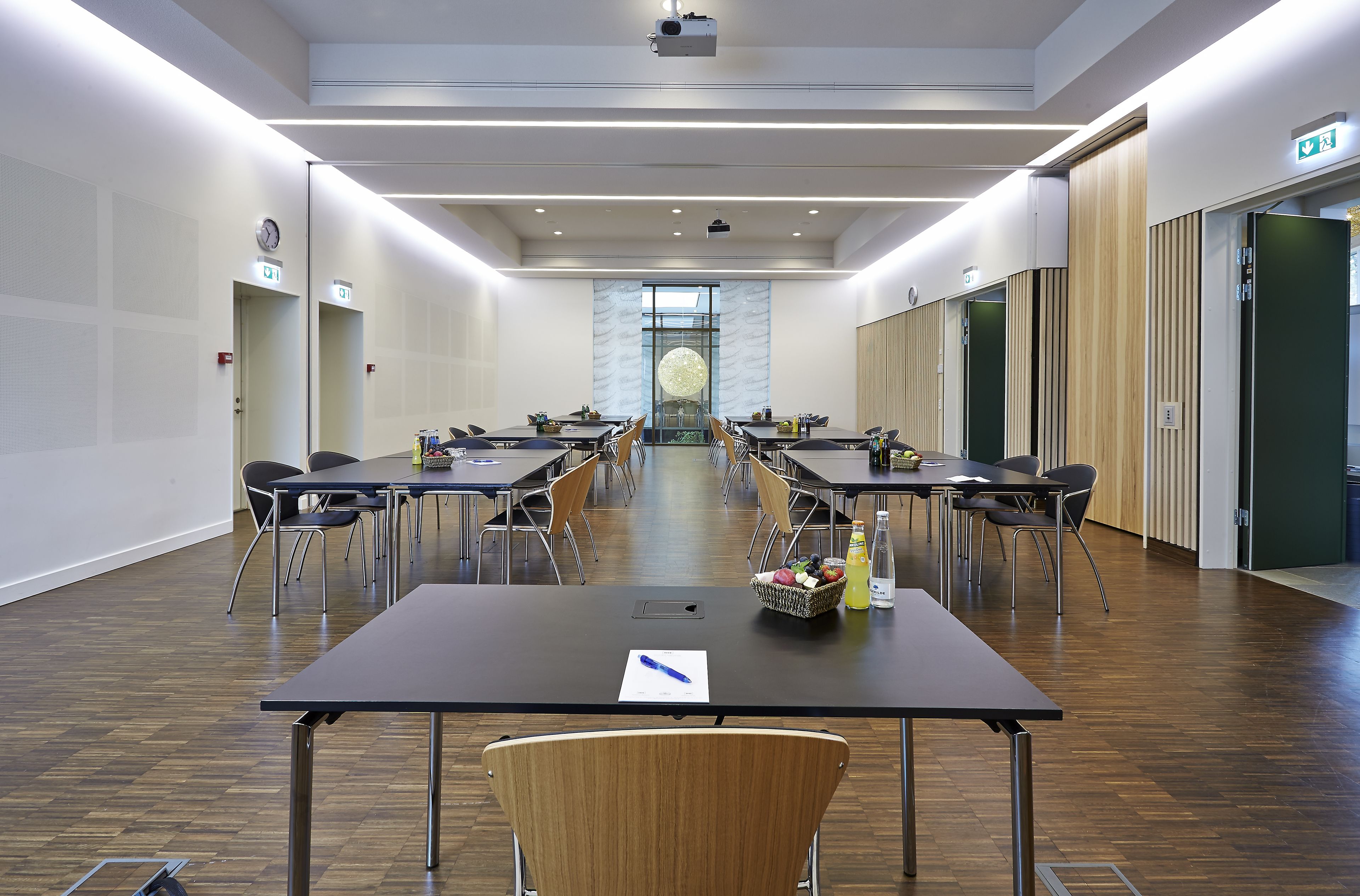 A conference room with multiple tables and chairs, equipped with a projector and a clock on the wall.