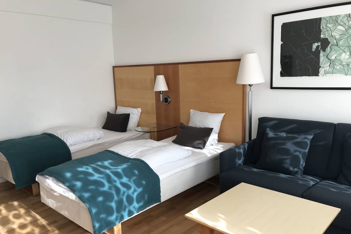 A hotel room with two beds, a sofa, a table, and a lamp.