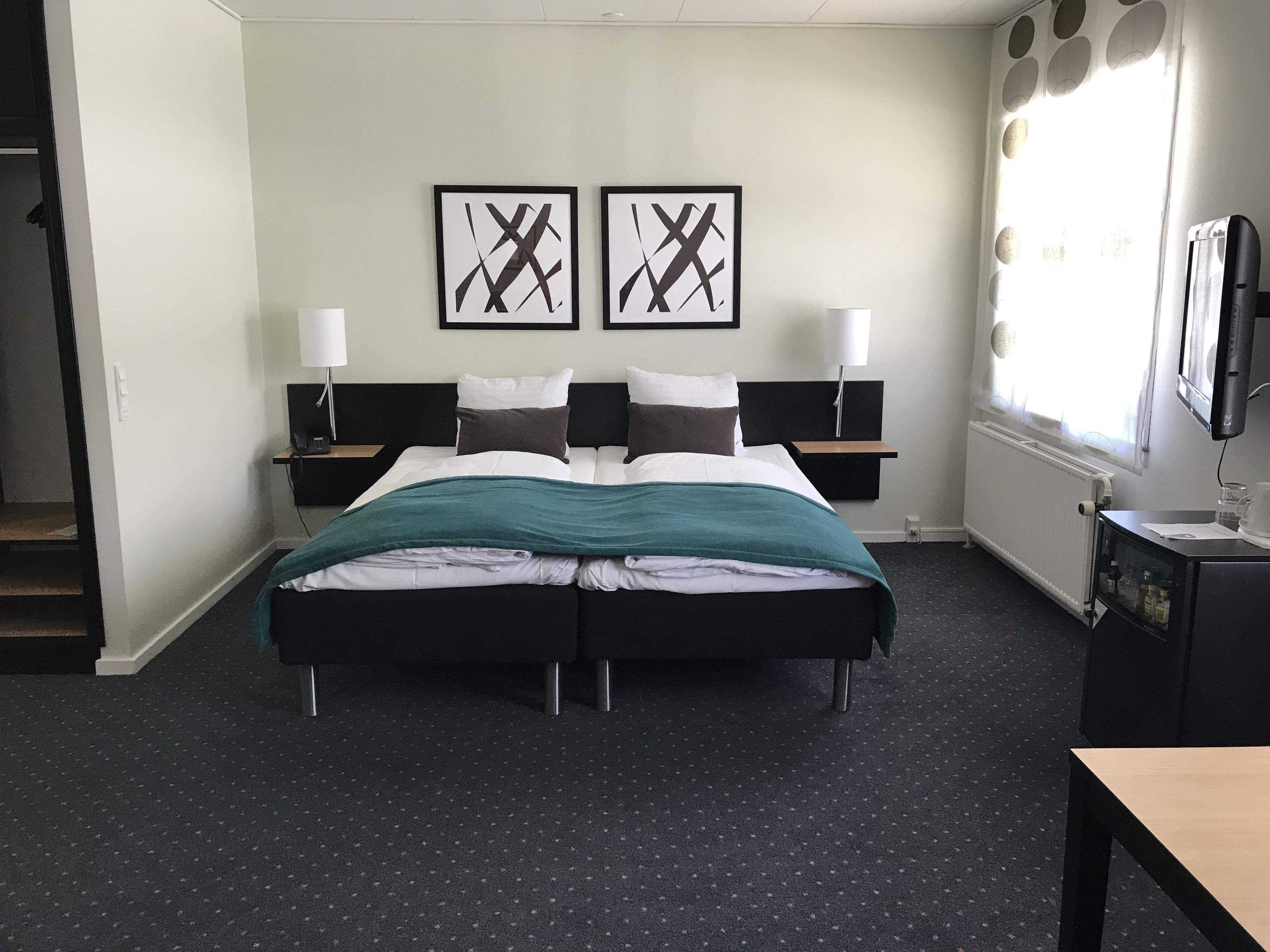 Una habitación de hotel con una cama doble, dos mesitas de noche, un televisor y una obra de arte en la pared.