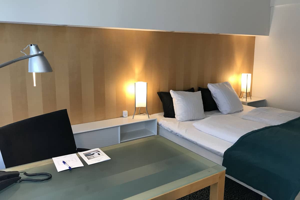 A hotel room with a bed, bedside tables, a desk, and a lamp.