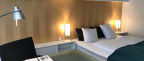 A hotel room with a bed, bedside tables, a desk, and a lamp.