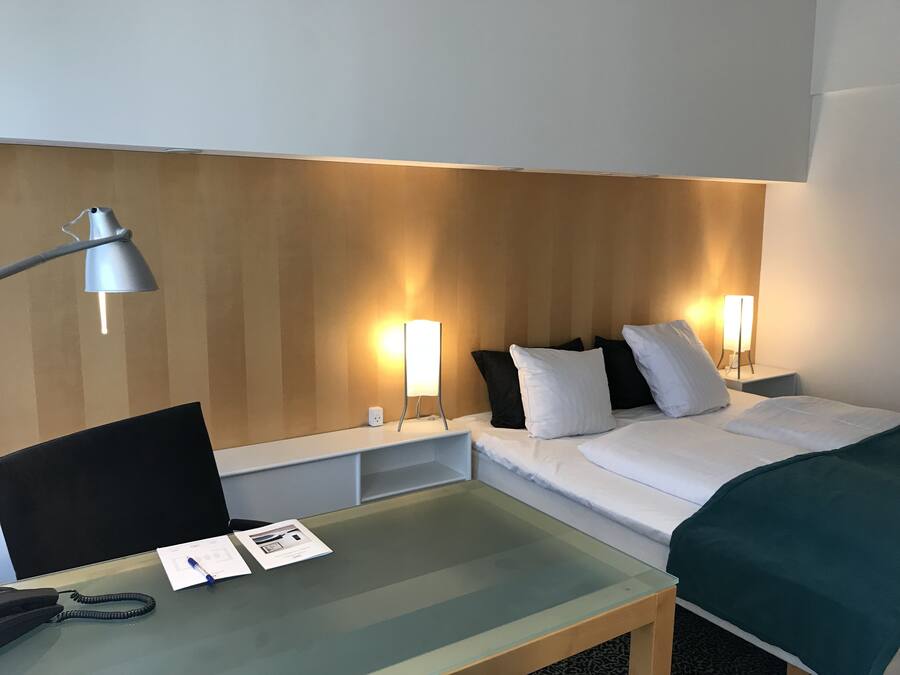 A hotel room with a bed, bedside tables, a desk, and a lamp.