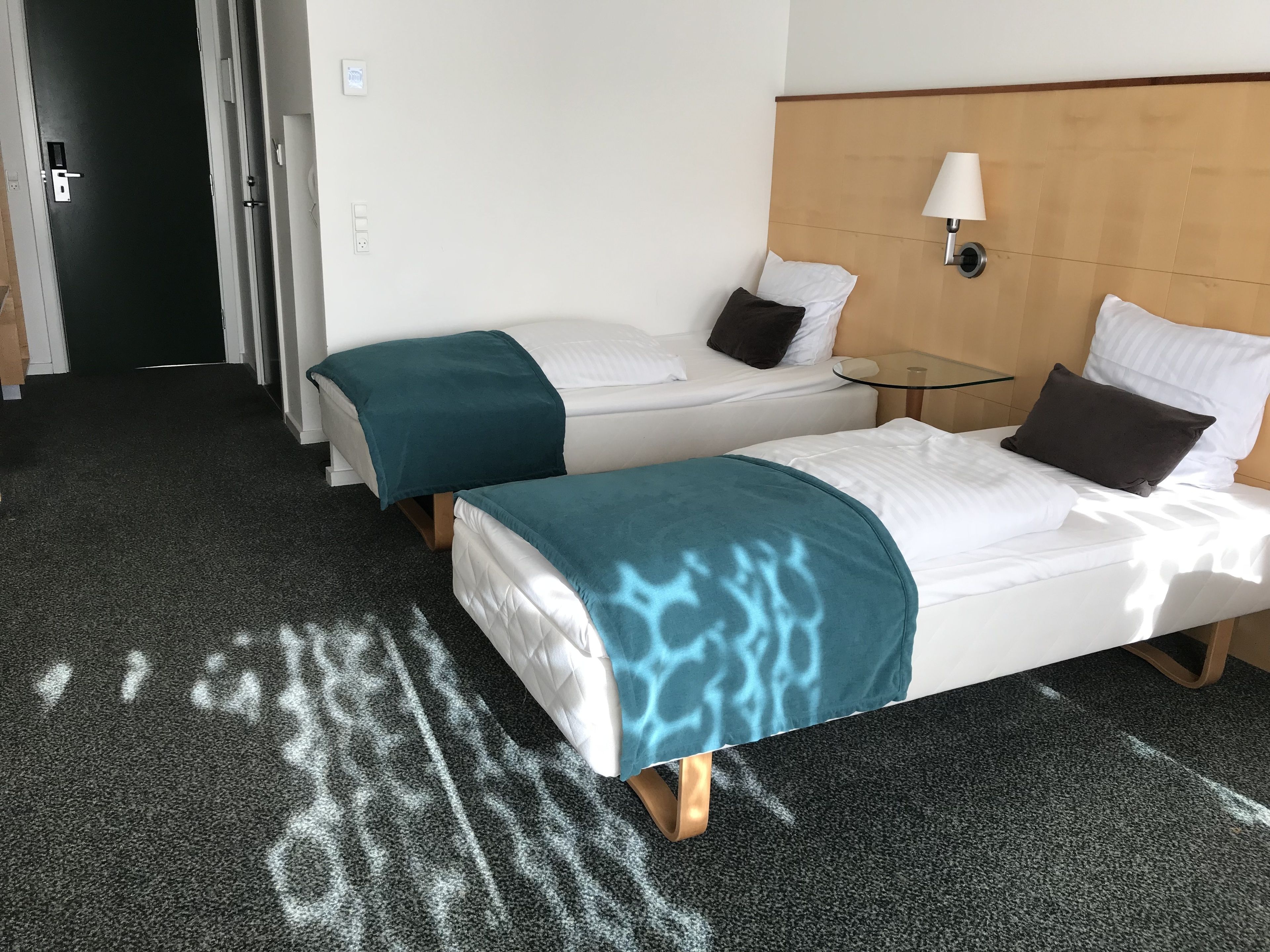 A hotel room with two beds, a small table, a lamp, and a door.