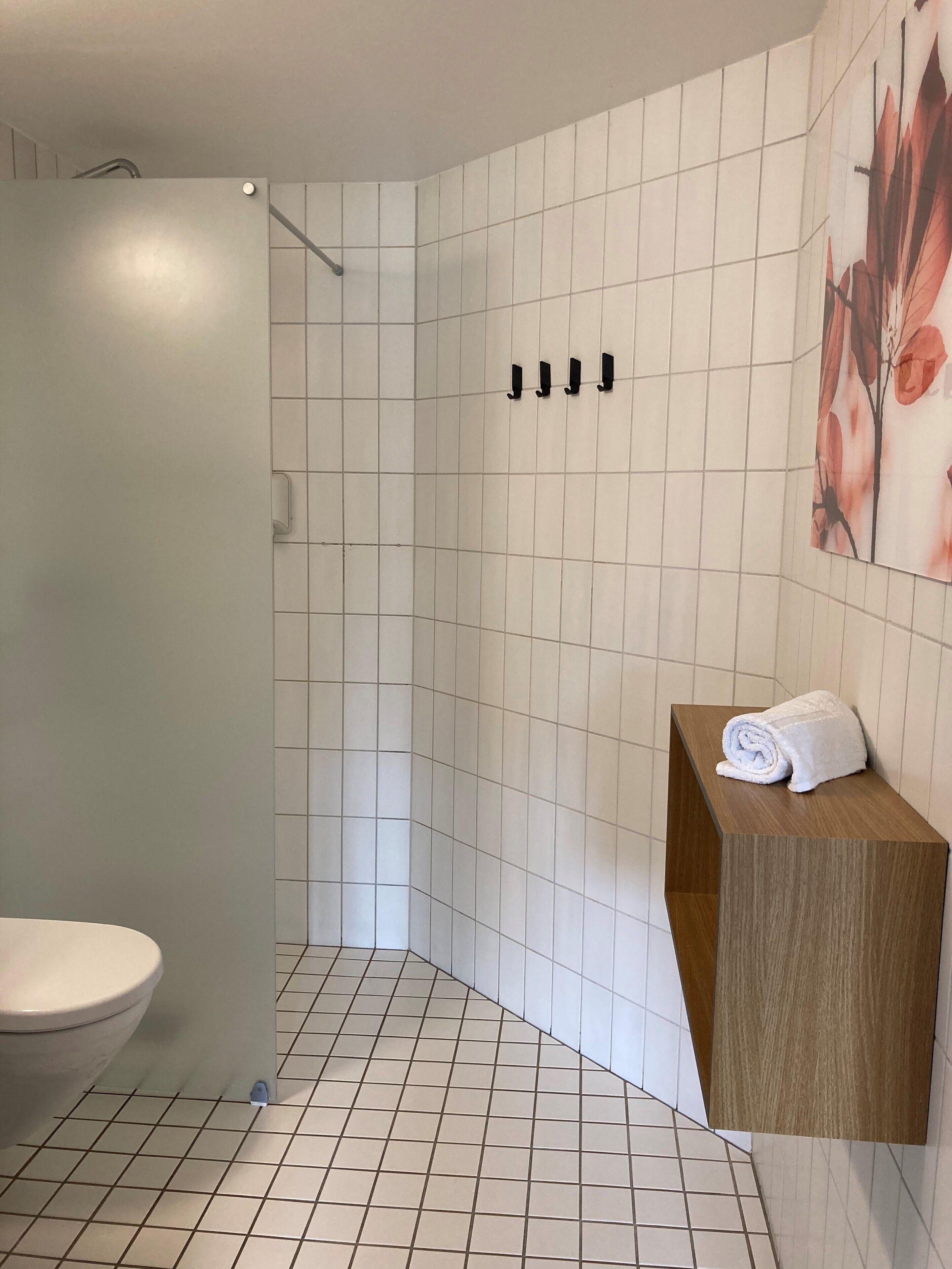 A modern bathroom with a white tiled floor, a wooden vanity with a towel, and a shower area.