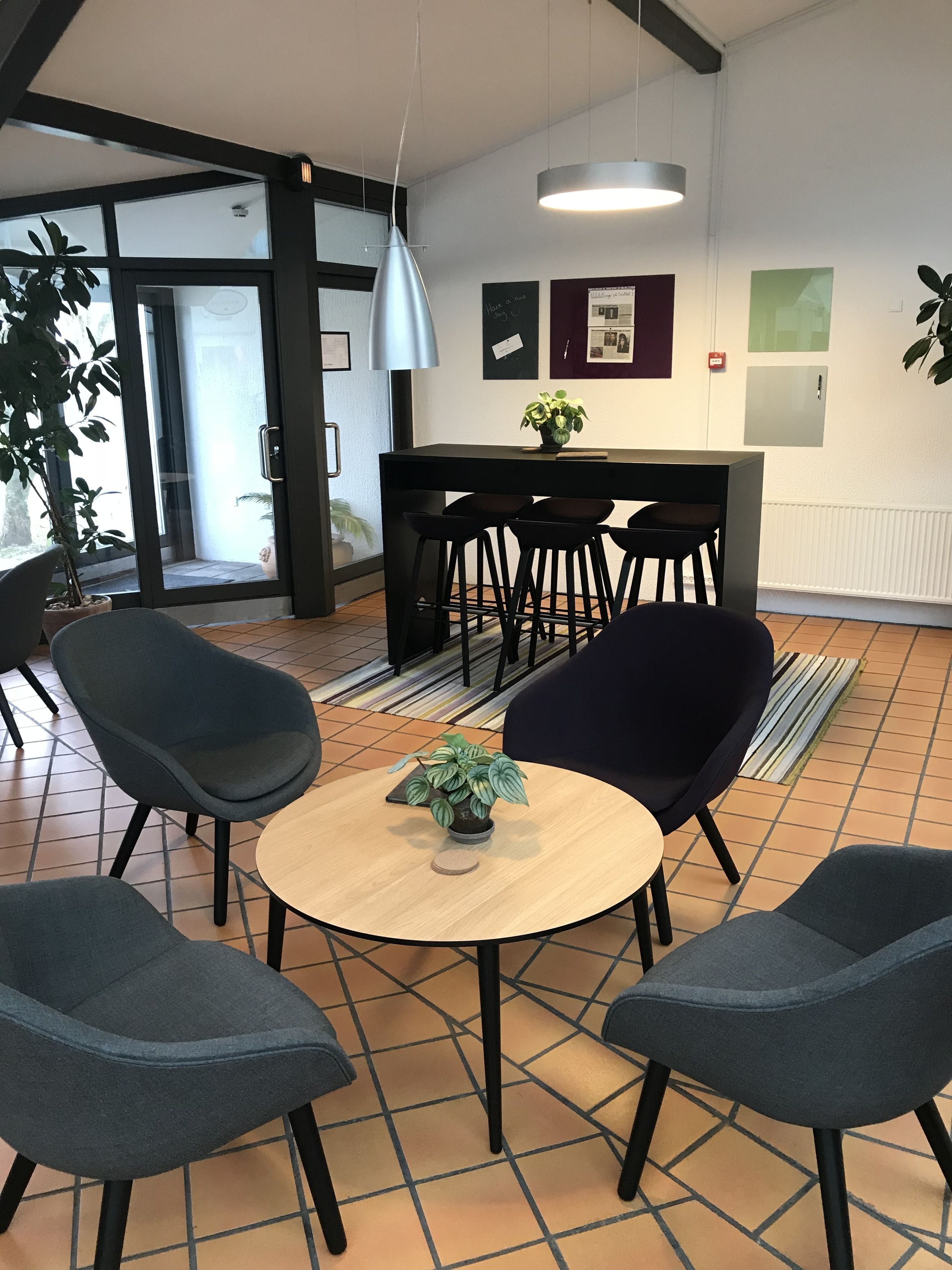 A modern interior with a round table, four chairs, a potted plant, and a bar area with stools.