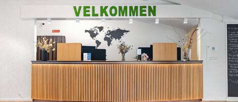 Una recepción con un cartel que dice 'VELKOMMEN', un mapa mundial y una pizarra con texto.