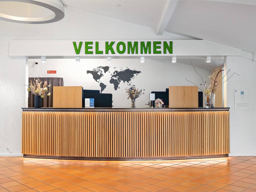 Una recepción con un cartel que dice 'VELKOMMEN', un mapa mundial y una pizarra con texto.