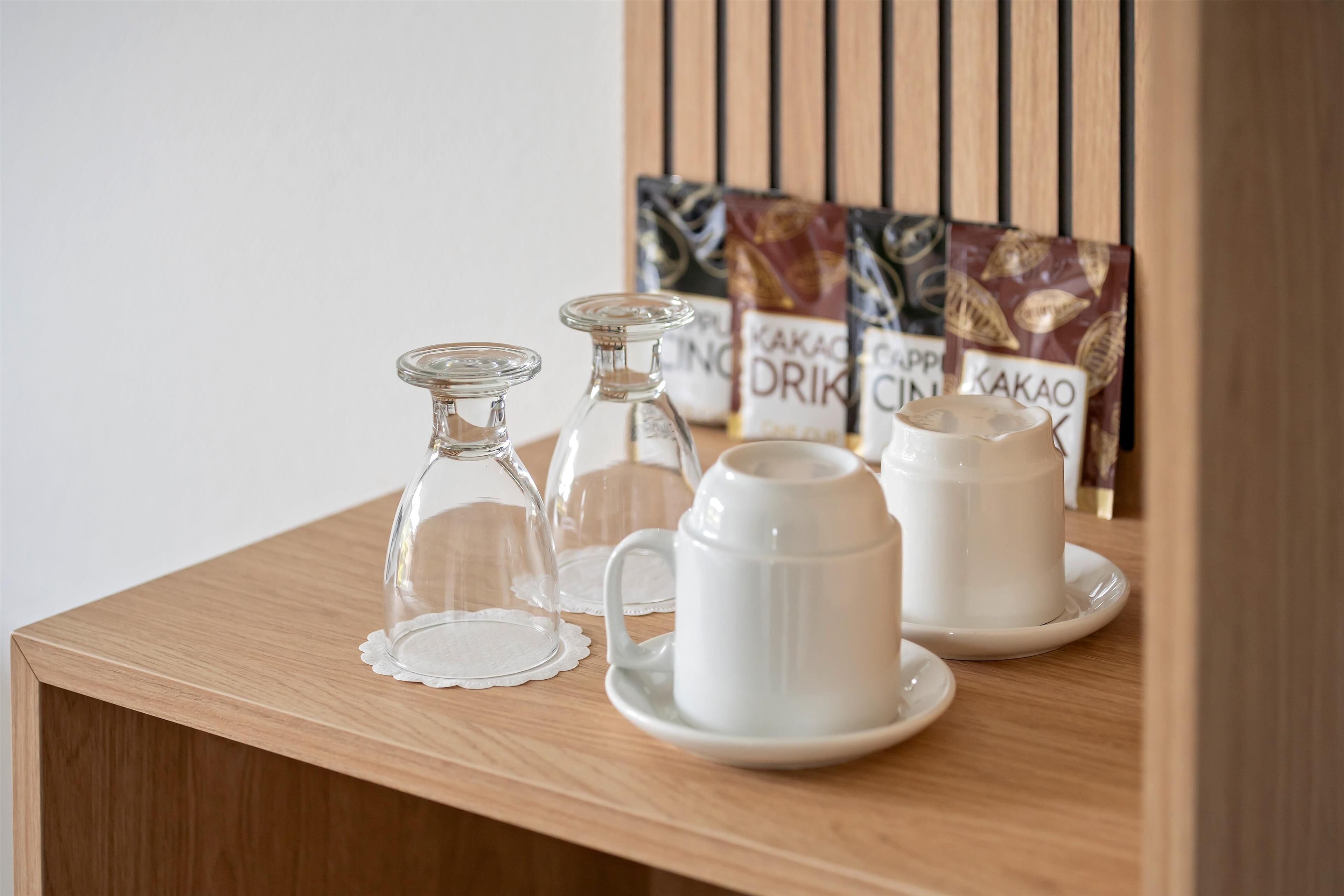 A wooden table with three glass decanters and two white ceramic cups and saucers.