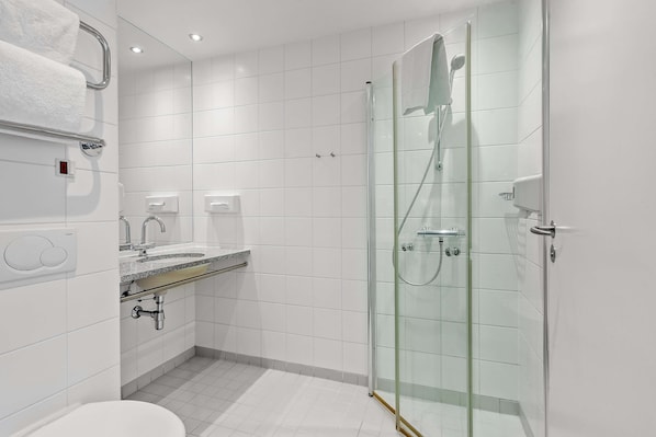 Un baño moderno con ducha envuelta en vidrio, un lavamanos con encimera de mármol y un inodoro.