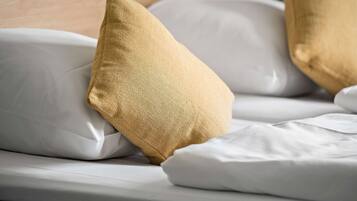Een bed met witte beddengoed en twee kussens, één goudkleurig en één wit.