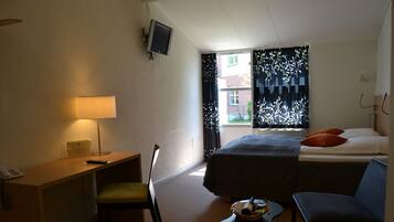 A hotel room with a bed, a desk, a chair, a small table, and a television.