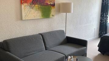 Una sala de estar moderna con un sofá gris, una mesita negra con una cesta, una lámpara de pie y un cuadro abstracto de colores en la pared.