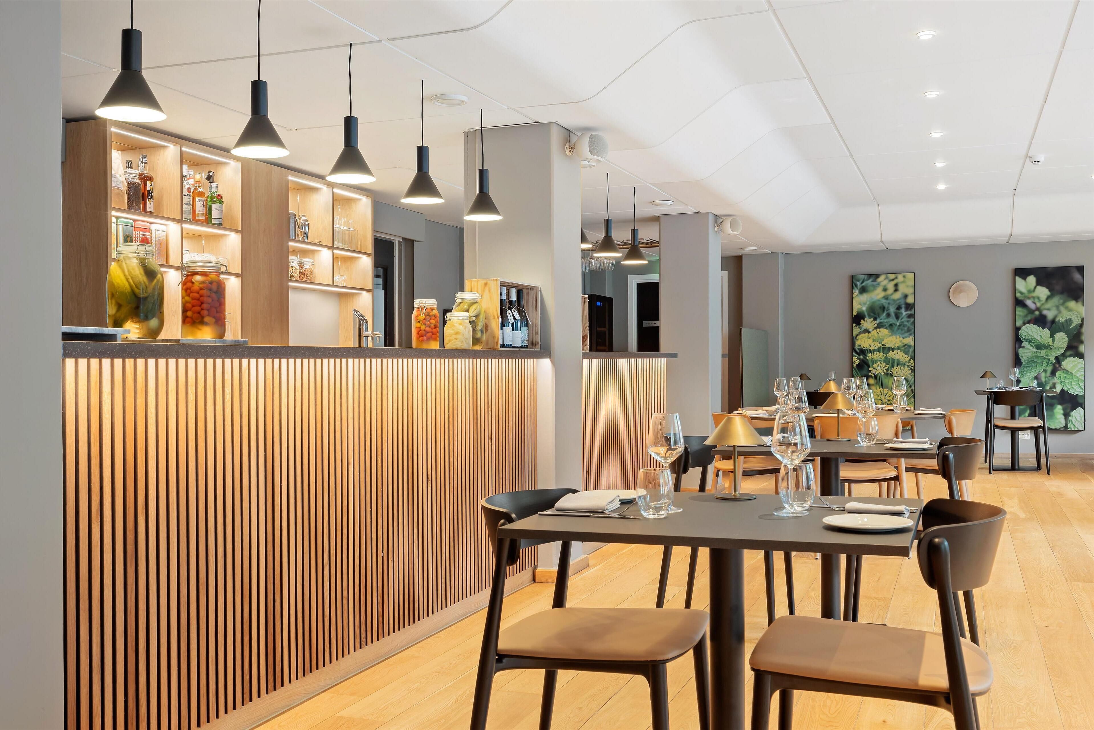 A modern restaurant interior with wooden paneling, pendant lighting, and neatly arranged tables and chairs.