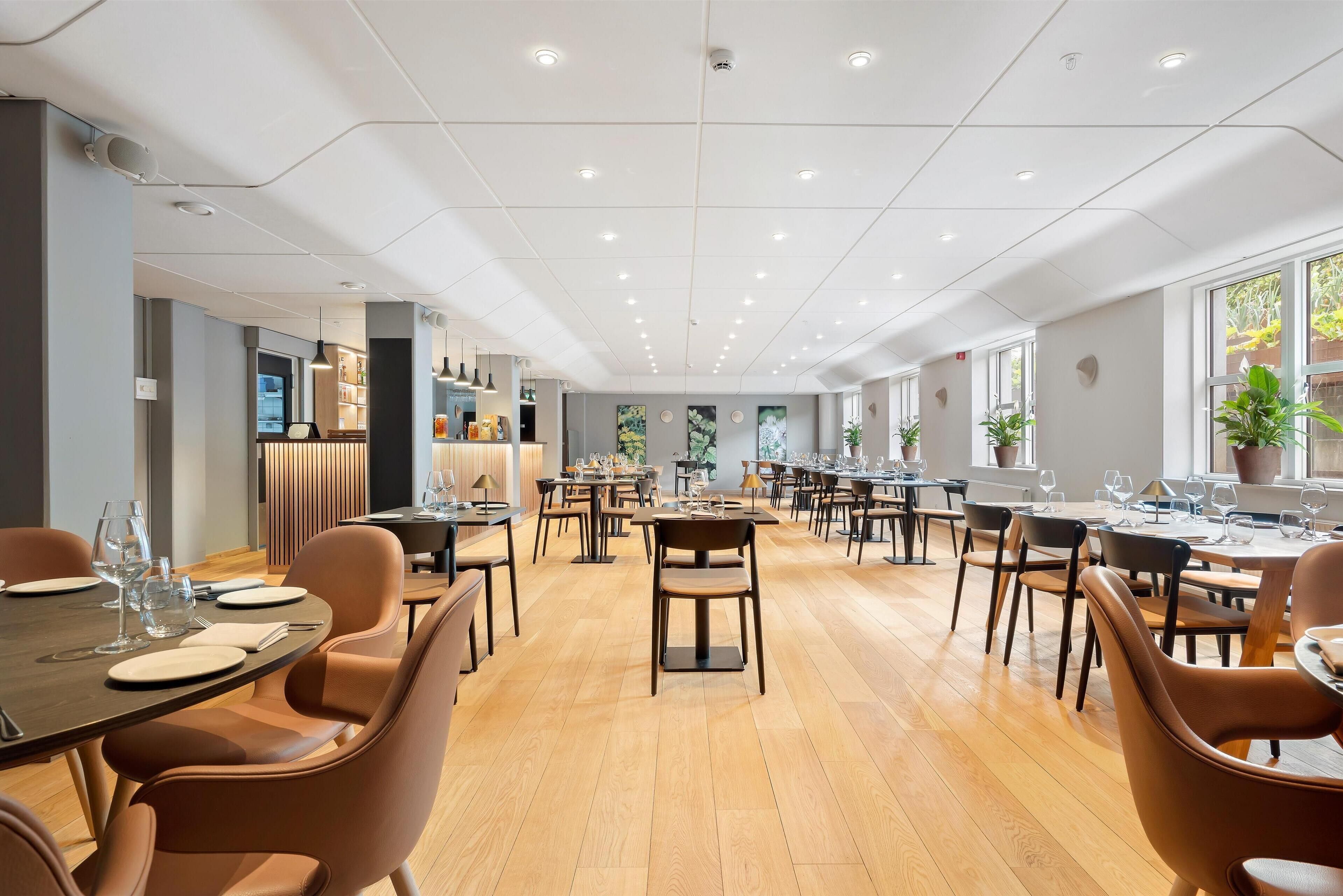 A spacious dining area with multiple tables and chairs, a modern ceiling design, and large windows allowing natural light.