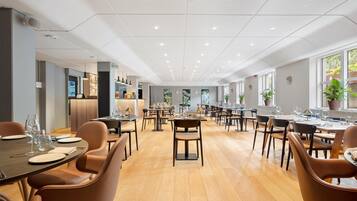 A spacious dining area with multiple tables and chairs, a modern ceiling design, and large windows allowing natural light.