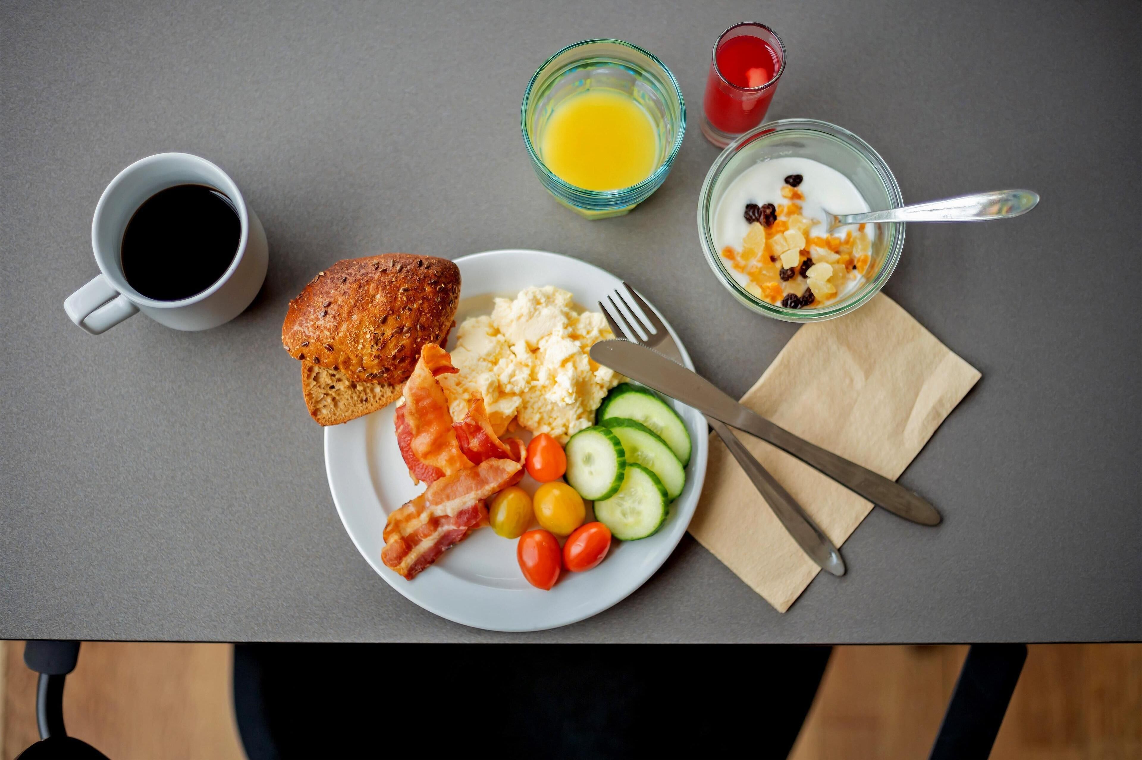 Een ontbijtbord met toast, spek, eieren, tomaten, komkommers en een glas sinaasappelsap.