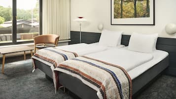Una habitación de hotel con una cama grande, una silla, un escritorio, una ventana con cortinas, una lámpara de pie y un cuadro en la pared.