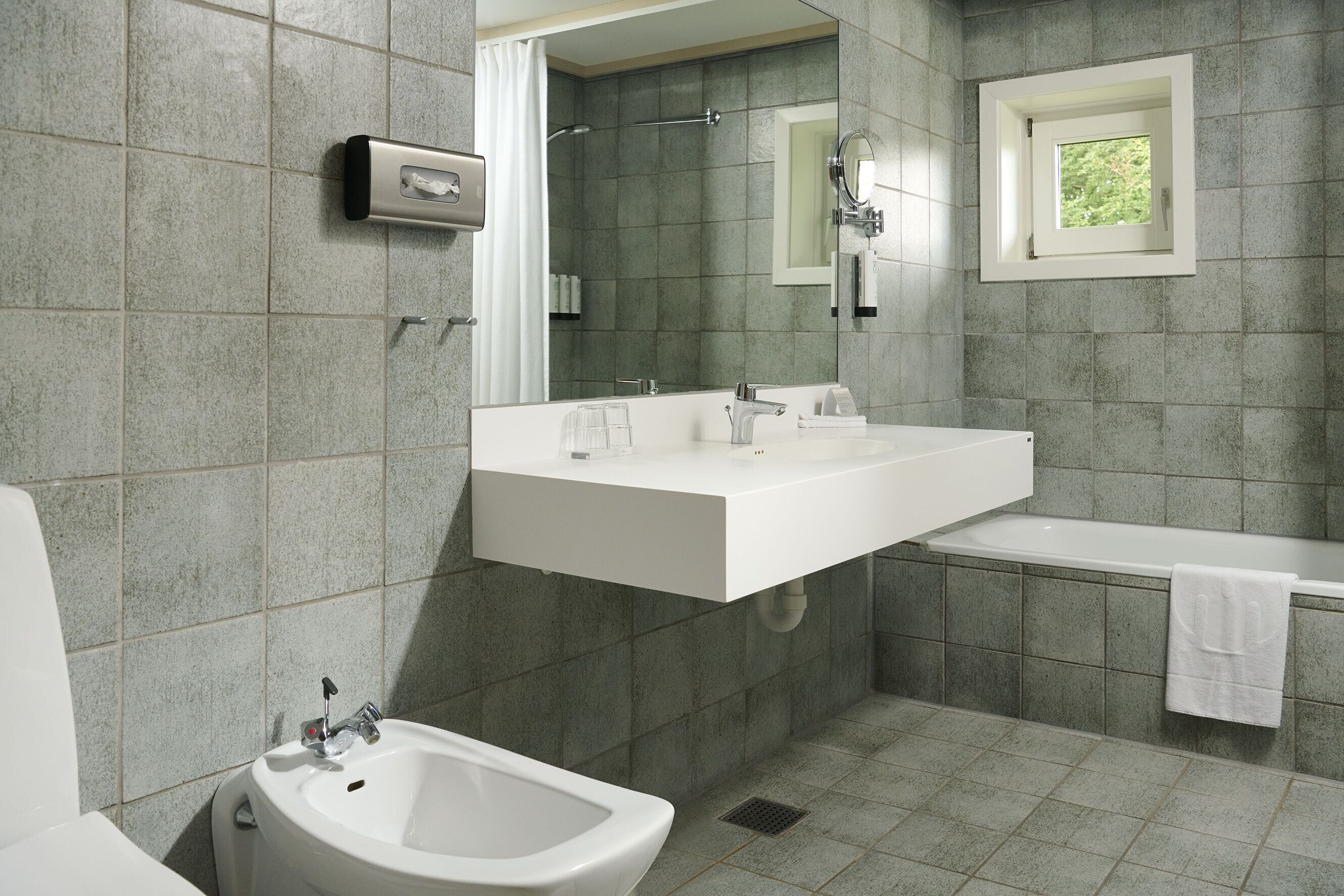 A modern bathroom with a bidet, a large mirror, a sink, and a bathtub.