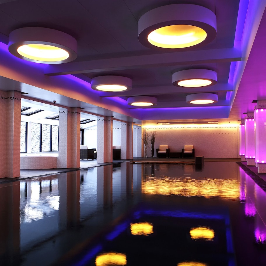 A modern hotel lobby with a reflective floor, large windows, and a reception area with purple lighting.