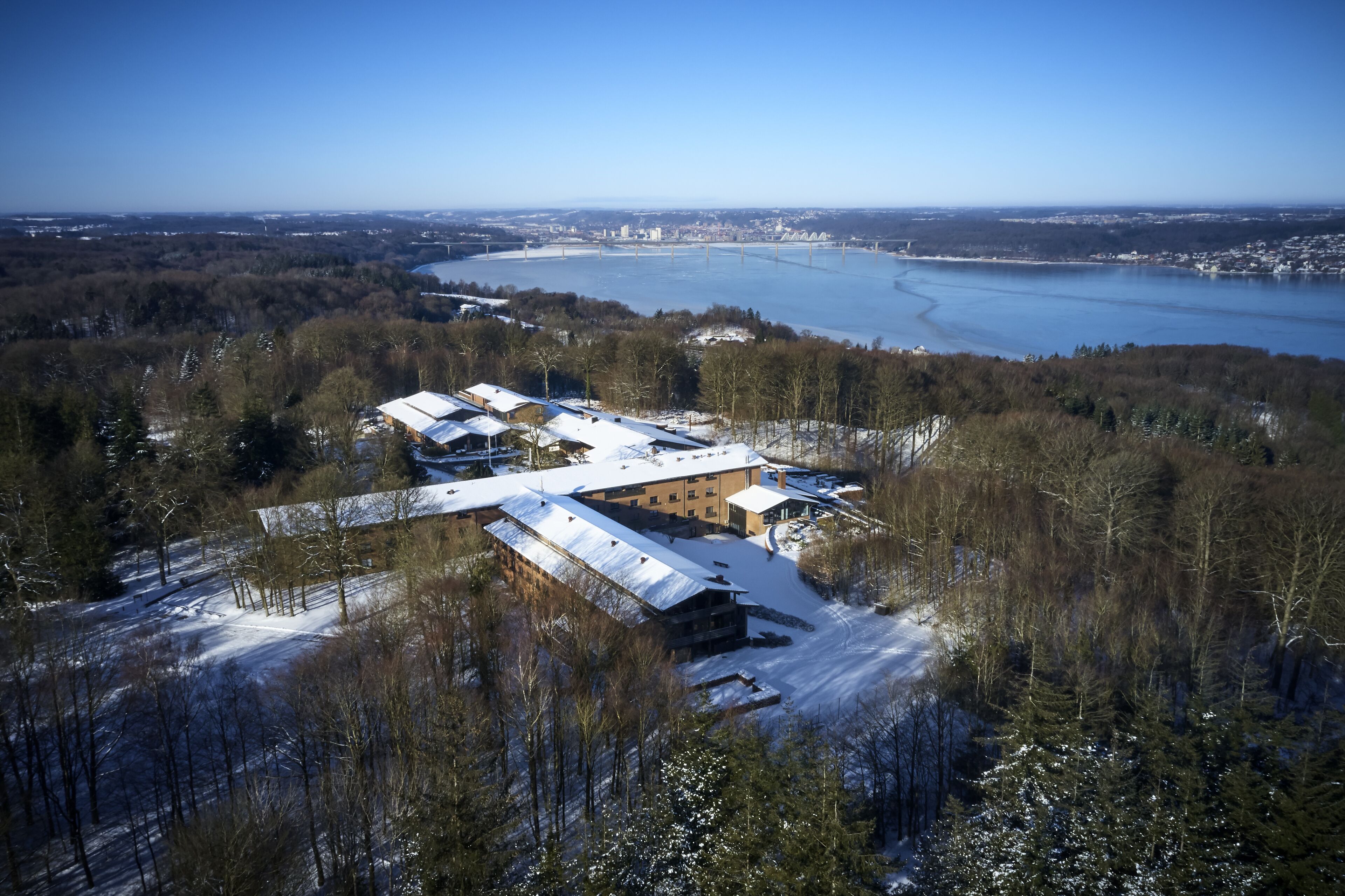 An aerial view of a building complex surrounded by snow-covered trees and a river.